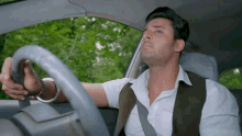 a man in a white shirt and brown vest driving a car