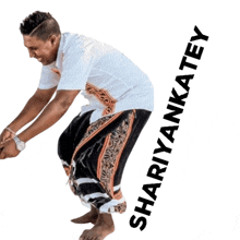 a man in a white shirt and black pants is squatting down with the name shariyankatey written below him