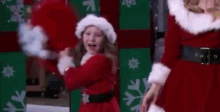 a little girl in a santa claus costume is dancing in front of santa claus .