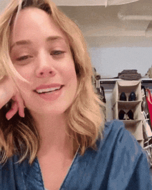 a woman in a blue shirt is smiling in a closet