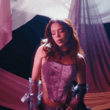 a woman in a purple corset and gloves stands in front of a pink curtain