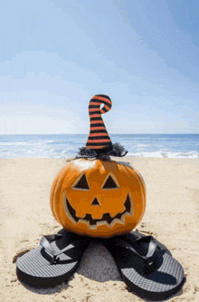 a pumpkin with a witch hat and flip flops on a beach