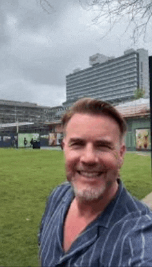 a man in a striped shirt is taking a selfie in a park with a building in the background .