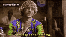 a man in a colorful shirt is sitting at a table and says i am a good for nothing .