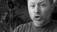 a man with a beard is wearing ear buds and making a funny face in a black and white photo .