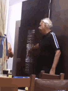 a man in a black shirt with blue stripes is standing in front of a wooden table .