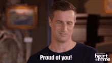 a man wearing a black shirt that says proud of you on it