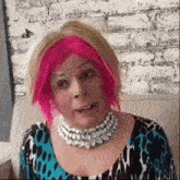 a woman with pink hair and a necklace is sitting on a couch and making a funny face .