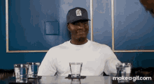 a man wearing a blue hat is sitting at a table with three glasses of water .