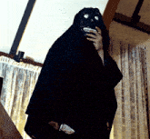 a person in a black cloak holding a knife in a room