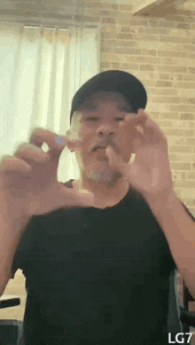 a man wearing a black shirt and a hat is holding something in his hands in front of a brick wall .