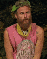 a man with a beard is wearing a pink tank top with the word alpha on it