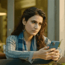 a woman in a blue sweater looks at her cell phone