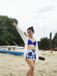 a woman in a bikini stands on a beach with a boat in the background with the number 25