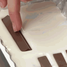 a person is dipping a kitkat bar into a tray of white chocolate