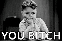 a black and white photo of a little boy sitting at a desk with his hand on his chin and the words `` you bitch '' .