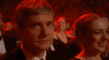 a man in a tuxedo and tie looks at a woman in a dress