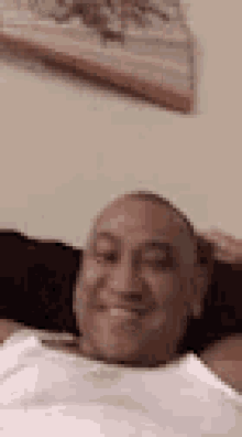 a man in a white tank top is smiling while laying on a couch with his hands behind his head .