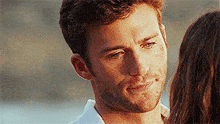 a man with a beard is smiling and looking at a woman on the beach .