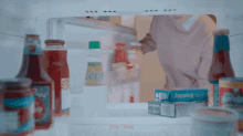 an open refrigerator with bottles of ketchup and a box of topping
