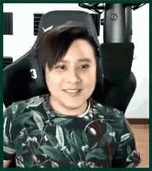 a man wearing headphones and a green shirt is sitting in a chair and smiling .