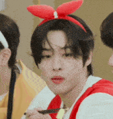 a young man wearing a red bunny ear headband is eating with chopsticks .