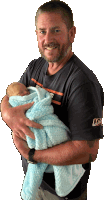 a man holding a baby wrapped in a blue blanket with a new era shirt on
