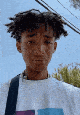a young man with dreadlocks is wearing a white shirt and a black strap