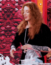 a woman with red hair is holding a plastic bag in front of a red wall .