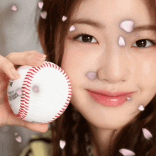 a woman holds a baseball in front of her face with petals falling around her