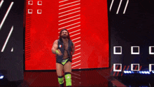 a wrestler with a beard is walking on a stage with a red background
