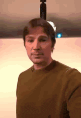 a man in a brown sweater is taking a selfie with a tripod on his head .
