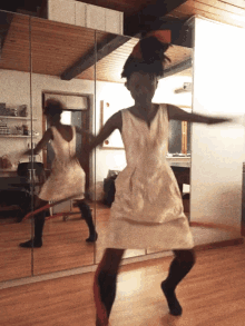 a woman in a white dress is dancing with a hula hoop in front of a mirror