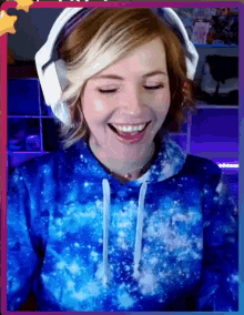 a woman wearing a blue tie dye hoodie and white headphones is smiling