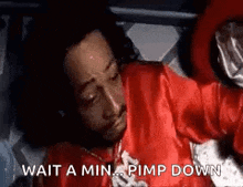 a man in a red shirt is laying on a bed with the words `` wait a min ... pimp down '' written on it .