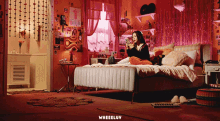 a woman sits on a bed in a bedroom with the word wheeluv on the bottom right