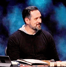a man with a beard is sitting at a desk with a tablet and a book