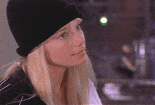 a blonde woman wearing a black beanie looks at the camera