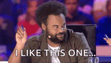 a man with a beard is sitting in front of a microphone and saying `` i like this one ... '' .