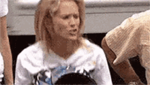 a woman in a white shirt is sitting in front of a group of people and making a face .