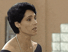 a woman wearing a pearl necklace and earrings looks to the side