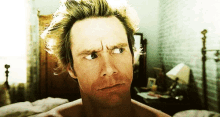 a man with messy hair is looking at the camera in a bedroom