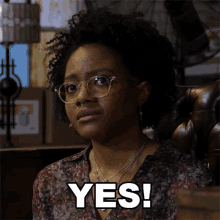 a woman wearing glasses is sitting in a chair with the word yes on her face