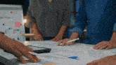 a group of people are gathered around a table with papers and a white board that says business plan on it