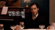 a man sits at a table with a glass of wine in front of a piano and a sign that says " รอ อย "
