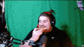 a man wearing headphones eating a sandwich in front of a green background