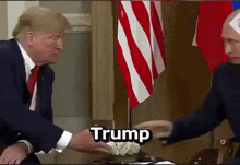 a man in a suit and tie is shaking hands with another man in front of an american flag and the word trump is visible
