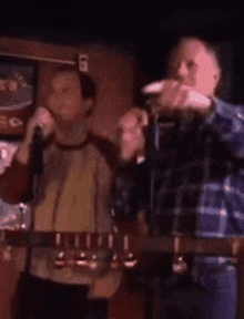 a man is singing into a microphone in a bar while another man looks on .