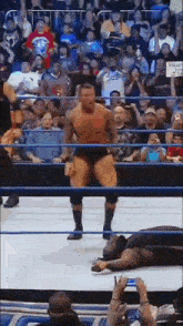 a man is standing in a wrestling ring in front of a crowd while another man is laying on the floor .