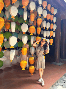 a woman in a hat stands in front of a wall of paper lanterns